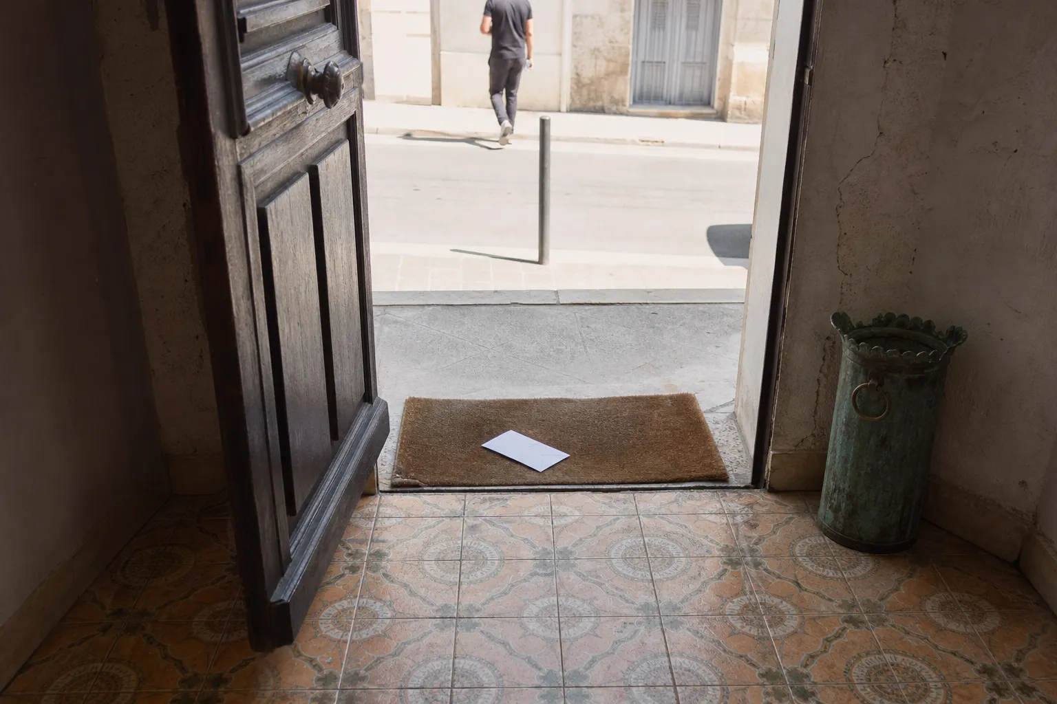 Porte d’entrée entrouverte vue depuis le couloir, prospectus sans marque retourné sur le paillasson