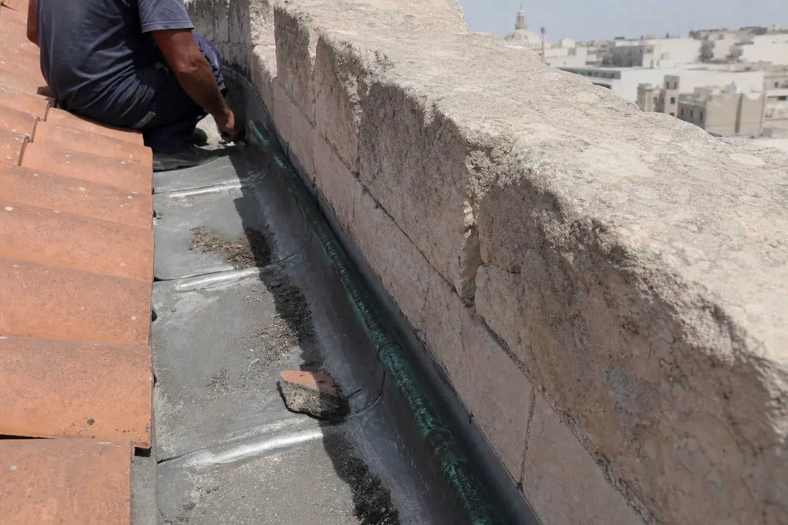 Gros plan sur un chéneau encaissé derrière un acrotère, chenal de zinc soudé avec un dépôt de limon au fond