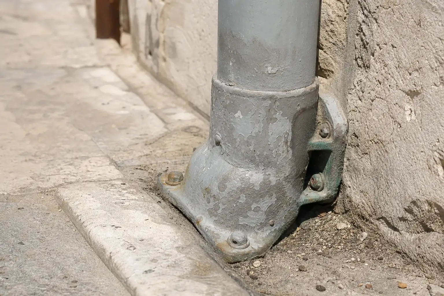 Gros plan sur un dauphin en fonte au pied d’une descente, évasement boulonné au mur et peinture écaillée