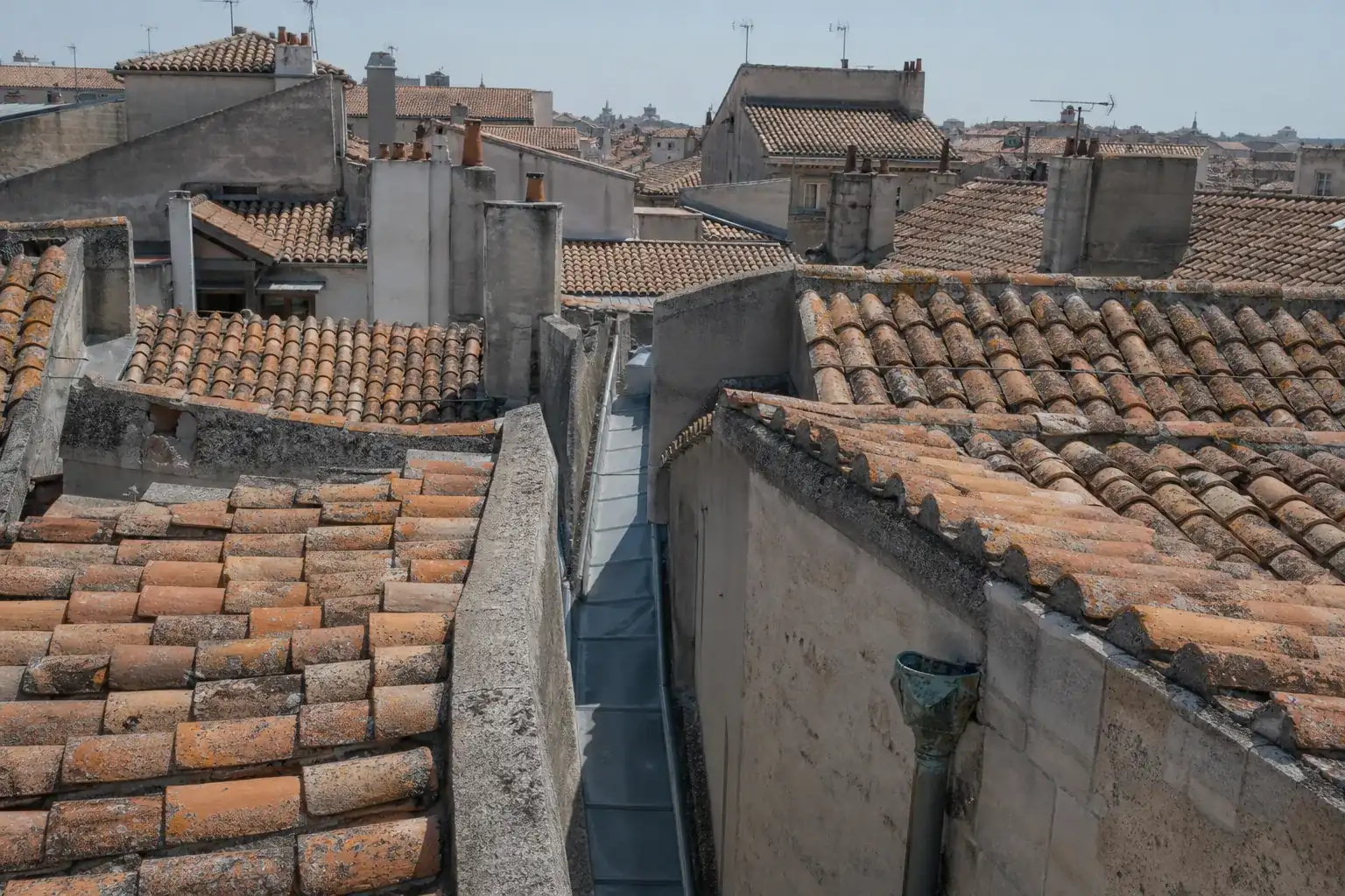 Toits de tuile canal d’un centre ancien vus d’une fenêtre de dernier étage, chéneau de zinc entre deux versants